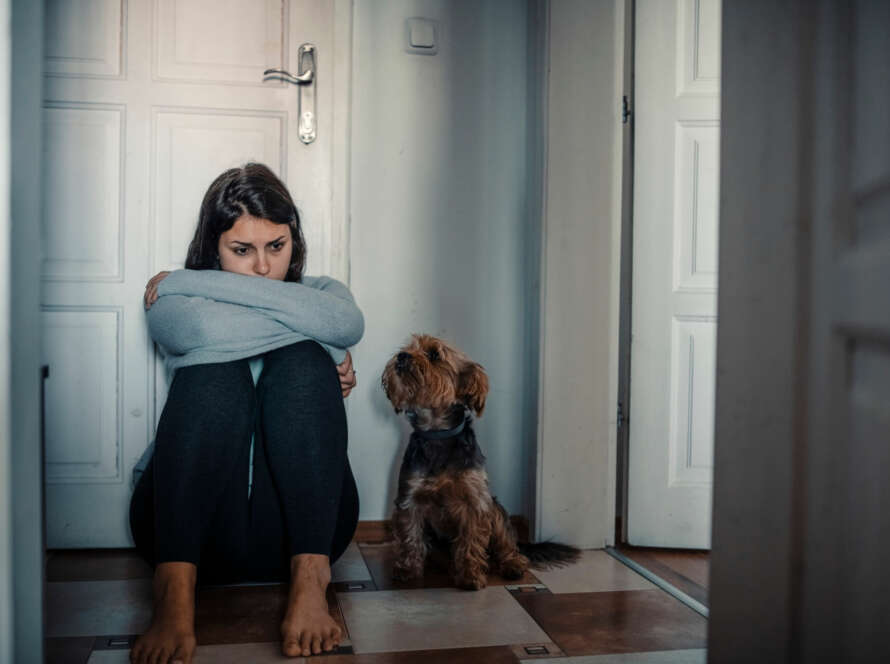 sad woman in crisis sitting against door with dog sitting next to her