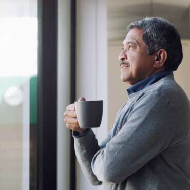 man looking out the window holding a cup of coffee