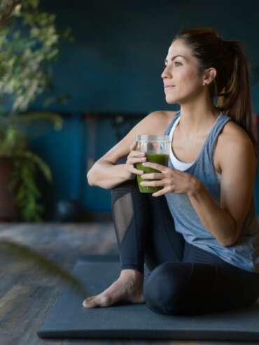 woman sitting on a yoga mat holding a green drink
