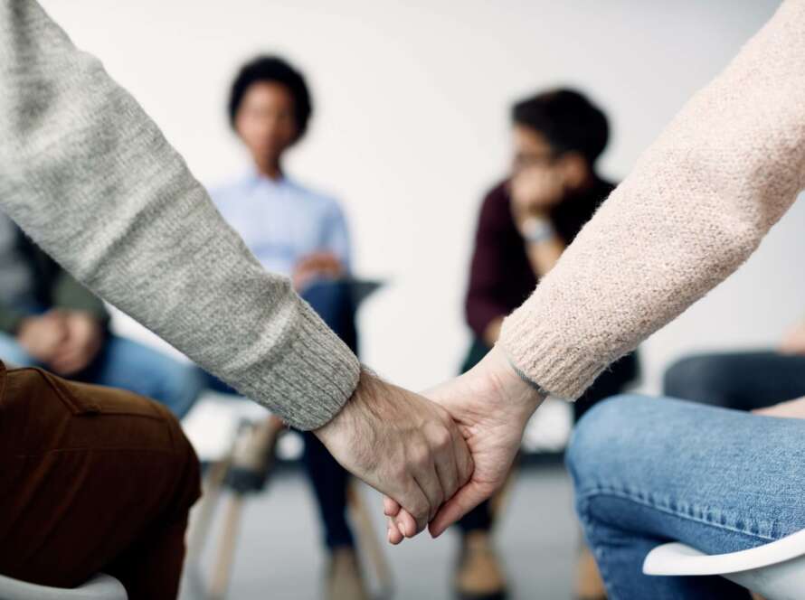 two people holding hands in a group counseling circle